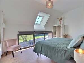 A bedroom with a skylight, a bed, a chair, a wardrobe, and a view of the outdoors. - L'Escale du Grand Bois (QUEBRIAC)