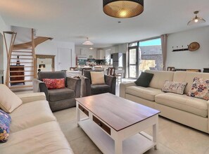 A modern living room with a sofa, armchair, coffee table, and a staircase. - L'Escale du Grand Bois (QUEBRIAC)