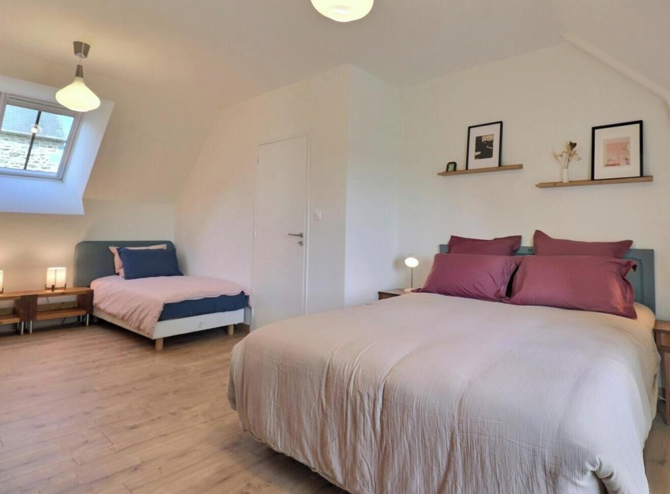 Ein Schlafzimmer mit zwei Betten, einem Oberlicht, einer Tür und Regalen an der Wand mit Bildern.