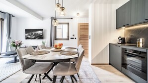 Eine moderne Küche mit Einbauofen, einem Essbereich mit Marmortisch und grau gepolsterten Stühlen sowie Pendelleuchten.