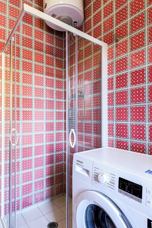 A bathroom with a red polka dot tiled wall, a white washing machine, and a shower enclosure. - El Sol by Casa di Marco (Campo Verde)
