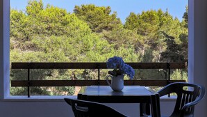 Een balkon met een tafel en stoelen, een plant in pot en uitzicht op bomen.