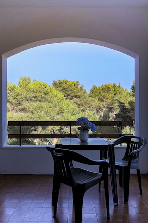 A balcony with a table and chairs, a potted plant, and a view of trees. - El Sol by Casa di Marco (Campo Verde)