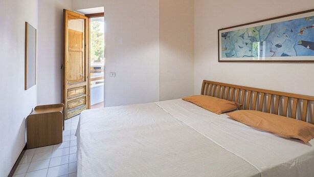 Een slaapkamer met een bed, een houten hoofdbord, een schilderij en een deur die uitkomt op een buitenruimte.