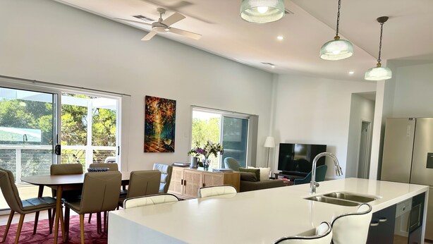 A modern kitchen with a central island, dining area with chairs, a TV, and a refrigerator.