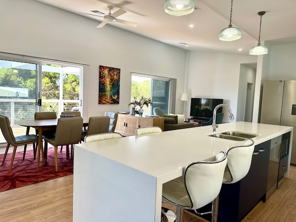 A modern kitchen with a central island, dining area with chairs, a TV, and a refrigerator.