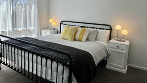 A neatly made bed with a black metal frame, white bedding, and two bedside tables with lamps.