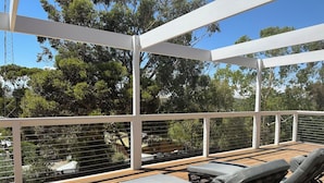 A wooden deck with two lounge chairs, a white pergola, and a view of trees and a fence.