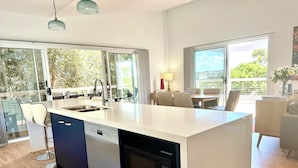 A modern kitchen with a dishwasher, a sink, and a dining area with a table and chairs.
