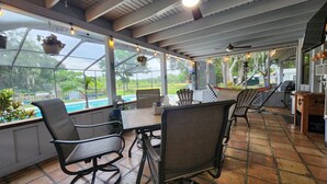 Uma varanda coberta com vista para a piscina, mobiliário de exterior e ventoinha no teto.