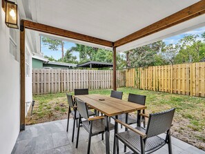 A covered patio with a wooden table and chairs, a wooden fence, and a view of the backyard. - Cool Blue - Designer 3BR Retreat (Fort Lauderdale)