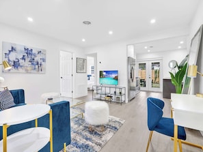 A modern living room with a TV, blue chairs, a white table, and a large painting. - Cool Blue - Designer 3BR Retreat (Fort Lauderdale)