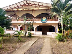 Un edificio de dos pisos con un porche, un letrero que dice 'Cocotoco's Lodore' y un jardín con palmeras.