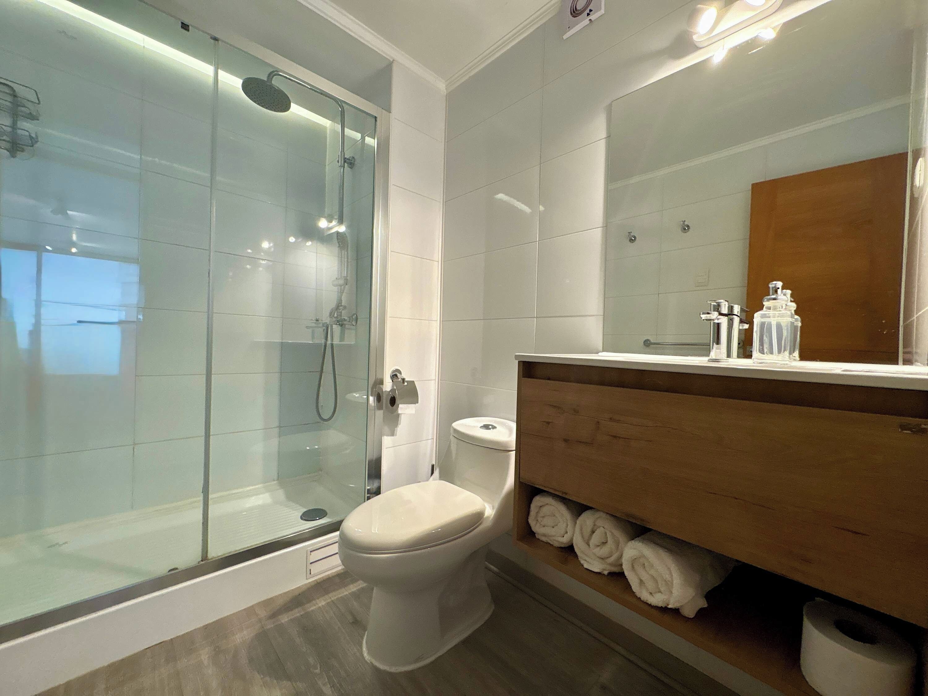 Ein modernes Badezimmer mit einer einachigen Duschkabine, einer Toilette und einem Waschtisch mit Handtüchern.