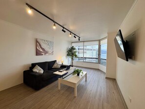 Een moderne woonkamer met een zwarte bank, een witte salontafel en een groot raam met uitzicht op gebouwen en water.