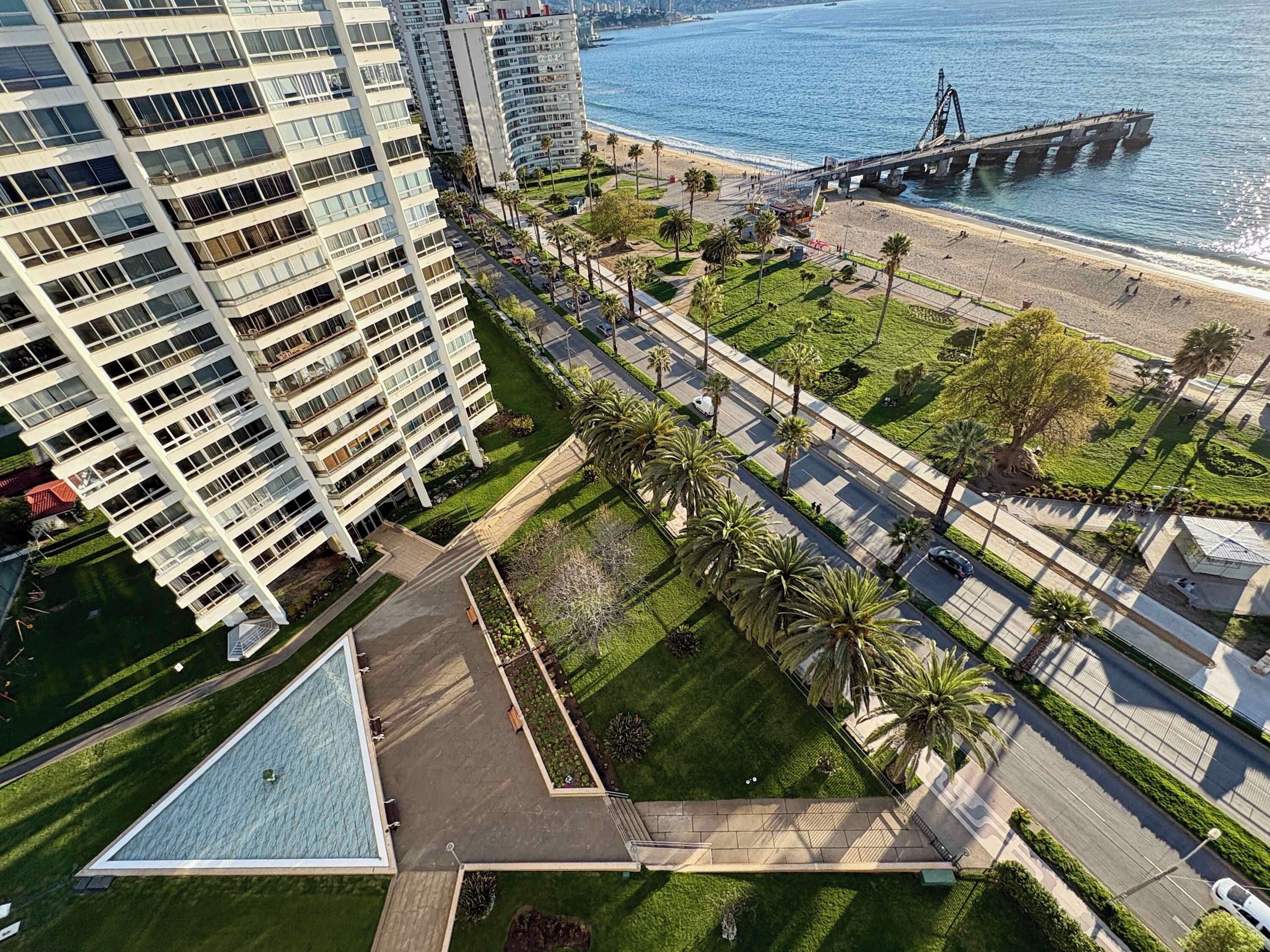 A high-rise building with a swimming pool, a pedestrian walkway, and a beach with a pier.