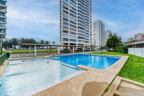 En swimmingpool med tilhørende terrasse, beliggende ved siden af høje boligbygninger.