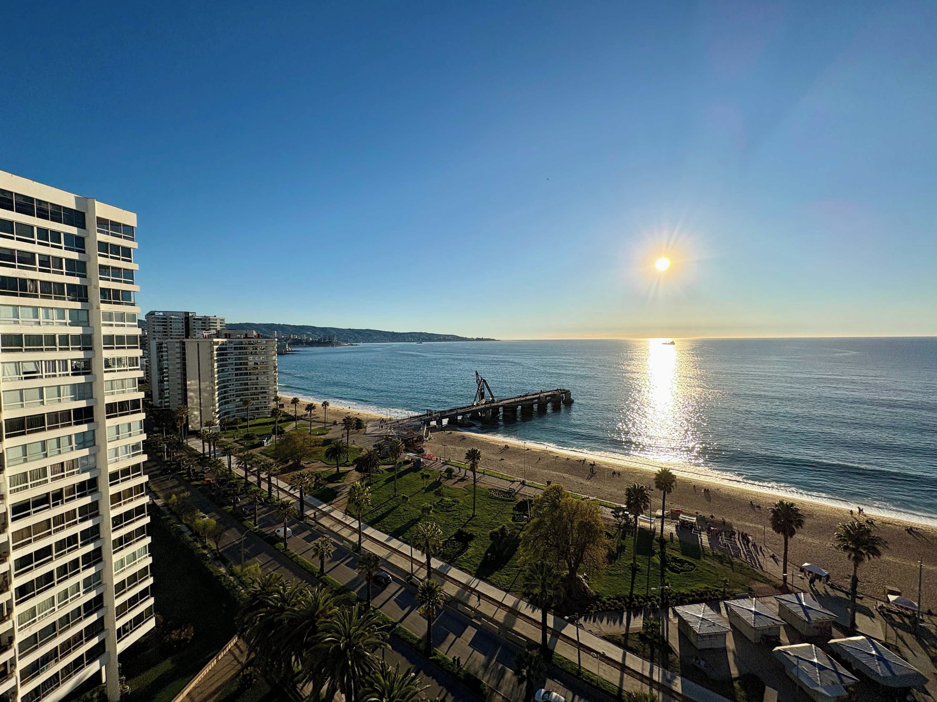 A coastal cityscape with a beach, a pier, and high-rise buildings.