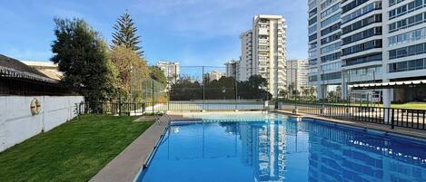 Piscina com cerca ao redor, junto a um edifício residencial alto.