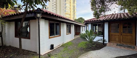 Un edificio residencial con fachada blanca y tejado de tejas rojas, rodeado de vegetación y un cielo despejado.