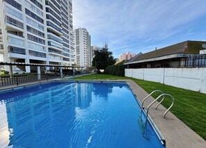 Ein Schwimmbecken mit Metallleiter, umgeben von einer weißen Mauer und einer Rasenfläche.