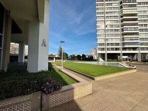 A modern building with a flat roof, a paved courtyard with a small pool, and a well-maintained lawn.