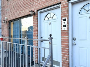 A brick building with two white doors, a metal gate, and a window with a metal grill. - Spacious and Stylish 3BR in North Bergen; 5 miles from NYC and MetLife stadium (North Bergen)