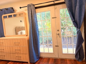 A room with a wooden dresser, a mirror, a sliding glass door with a view of greenery, and a curtain. - Spacious and Stylish 3BR in North Bergen; 5 miles from NYC and MetLife stadium (North Bergen)