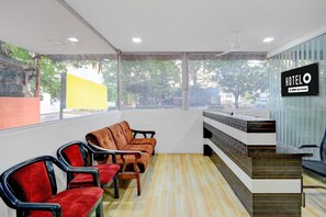 Un hall d’hôtel comprenant un comptoir d’accueil, un espace salon avec des fauteuils et de grandes fenêtres donnant sur la verdure.
