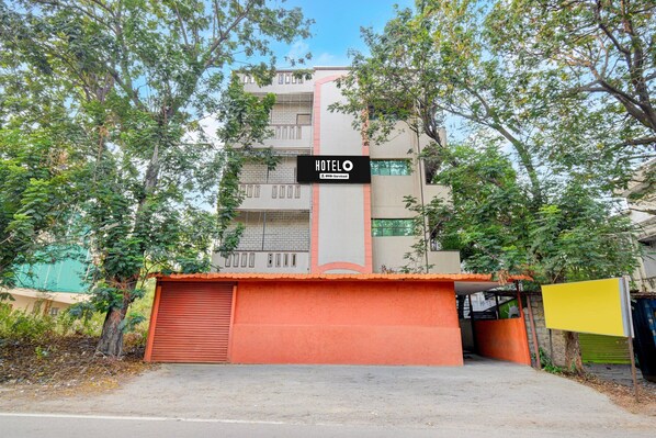 Un hôtel avec une enseigne indiquant « HOTELO », une porte de garage rouge et des arbres au premier plan.