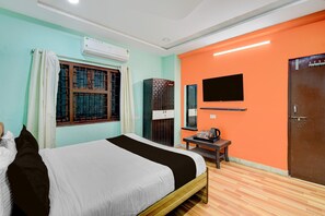 Une chambre à coucher comprenant un lit, un climatiseur, une fenêtre avec des rideaux, un téléviseur, une armoire et une porte.