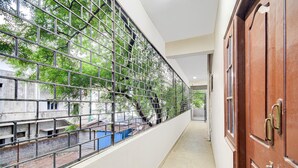 Un pasillo con cerca metálica, puerta de madera y vistas a edificios y árboles.