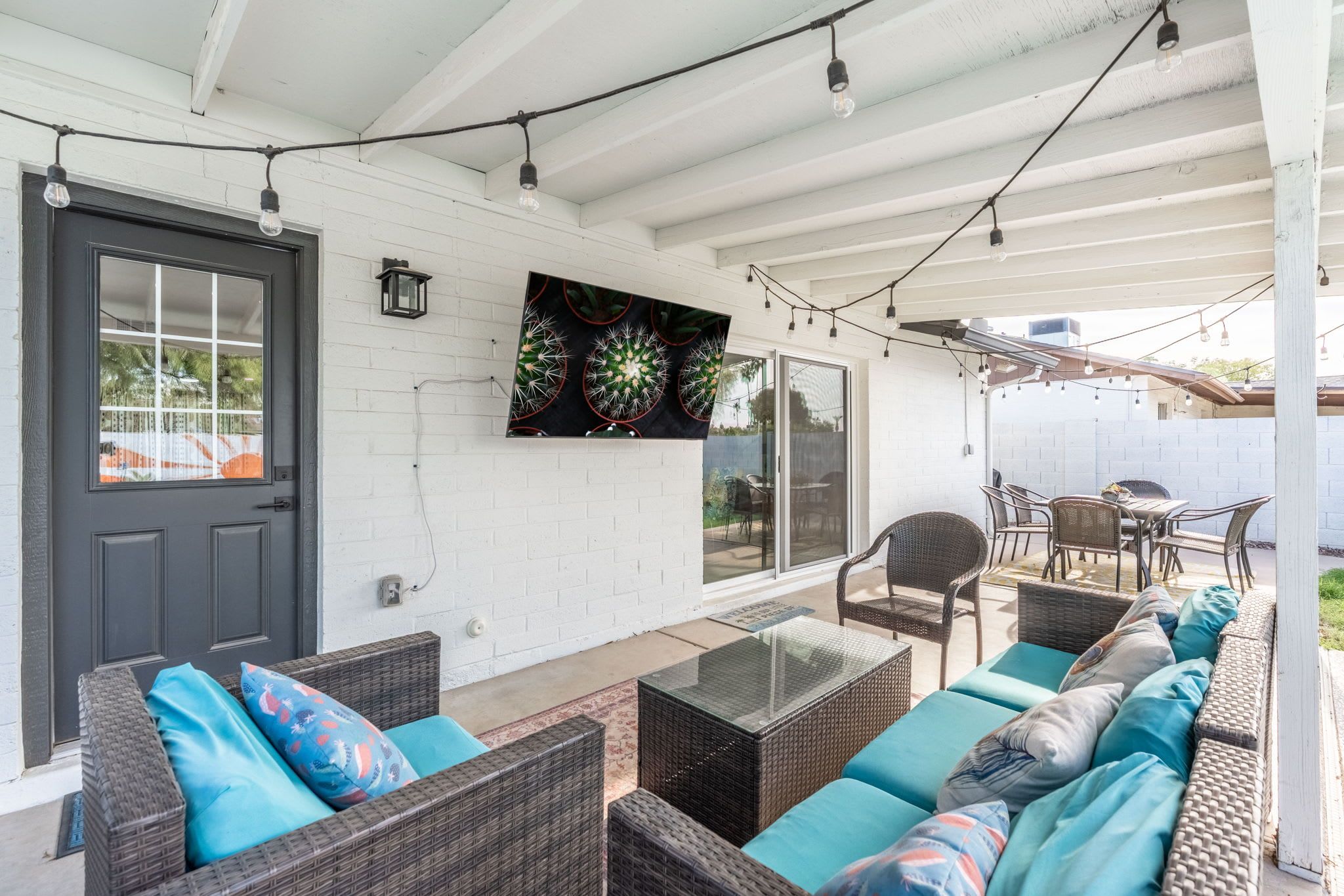 A covered patio with wicker furniture, a black door, and a cactus wall art piece.