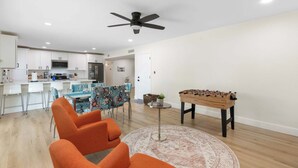 A modern living room with a foosball table, orange chairs, and a dining area with patterned tablecloths. - 3bd, Pool, Hot Tub, Garage, Full Kitchen, ASU (Tempe)