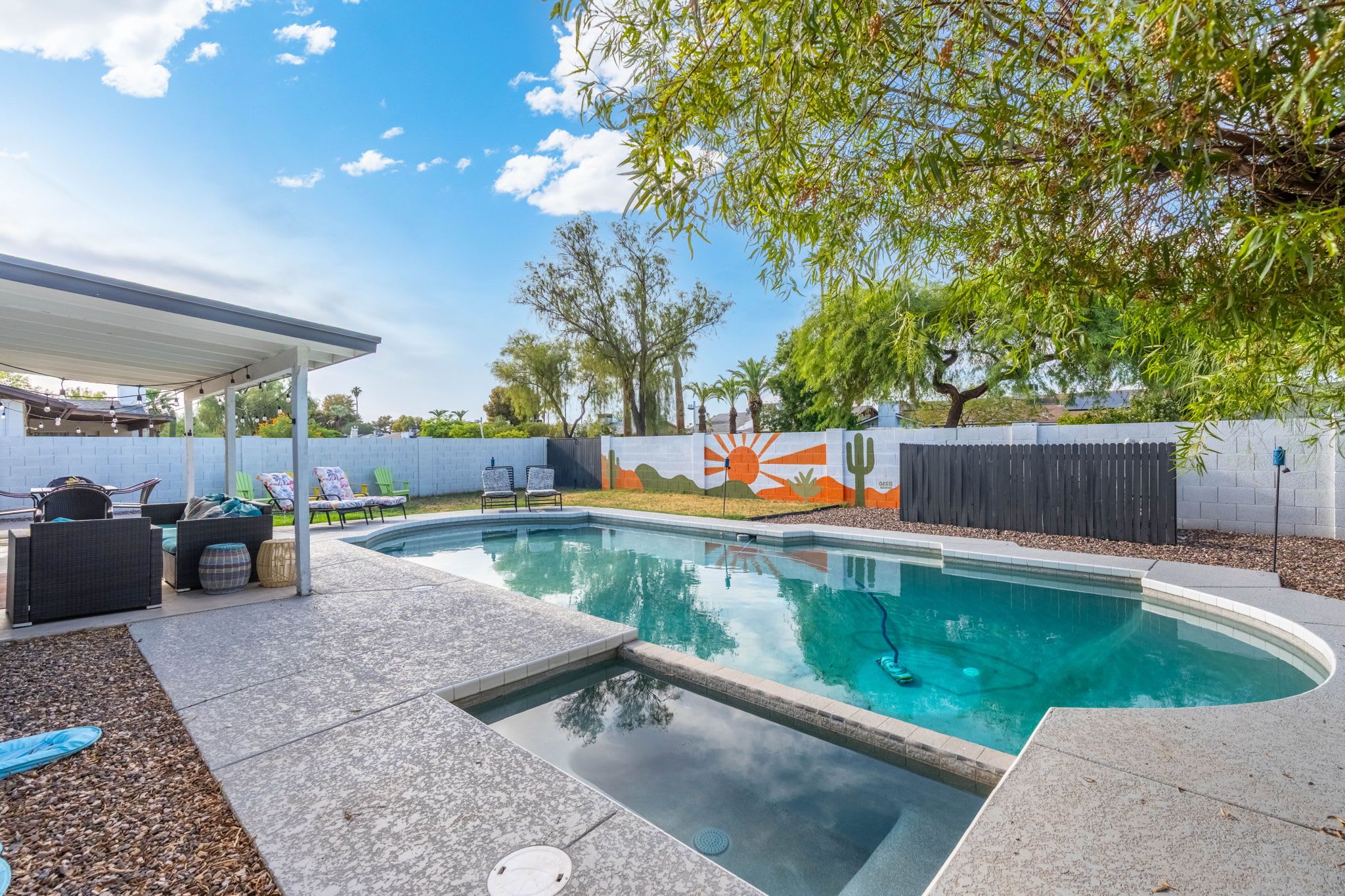 A backyard with a swimming pool, lounge chairs, and a covered patio area.
