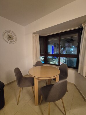 Ein Zimmer mit einem runden Holztisch, vier grauen Stühlen, einer Wanduhr und einem Fenster mit Blick auf die Stadt.