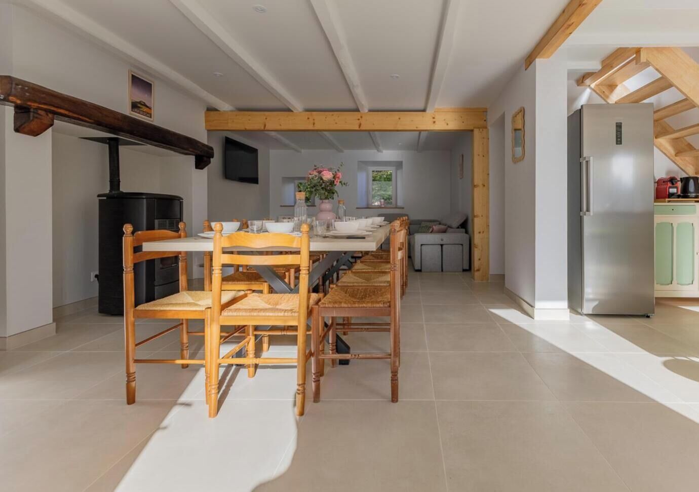 A modern kitchen with a dining area, wooden beams, a built-in stove, and a stainless steel refrigerator.