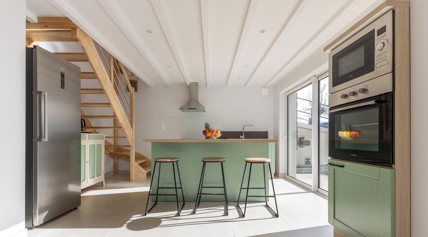 Una cocina moderna con horno empotrado, refrigerador y una escalera de madera.