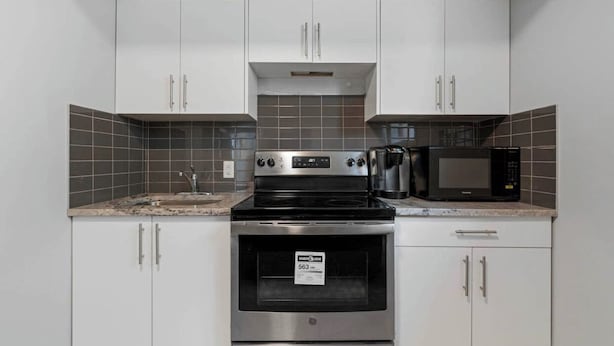 A kitchen with white cabinets, a stainless steel stove, a microwave, and a coffee maker.