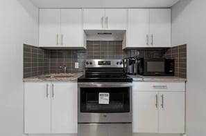 Une cuisine avec des meubles blancs, une cuisinière en acier inoxydable, un four à micro-ondes et une machine à café.