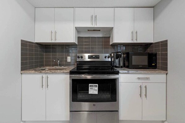 A kitchen with white cabinets, a stainless steel stove, a microwave, and a coffee maker.