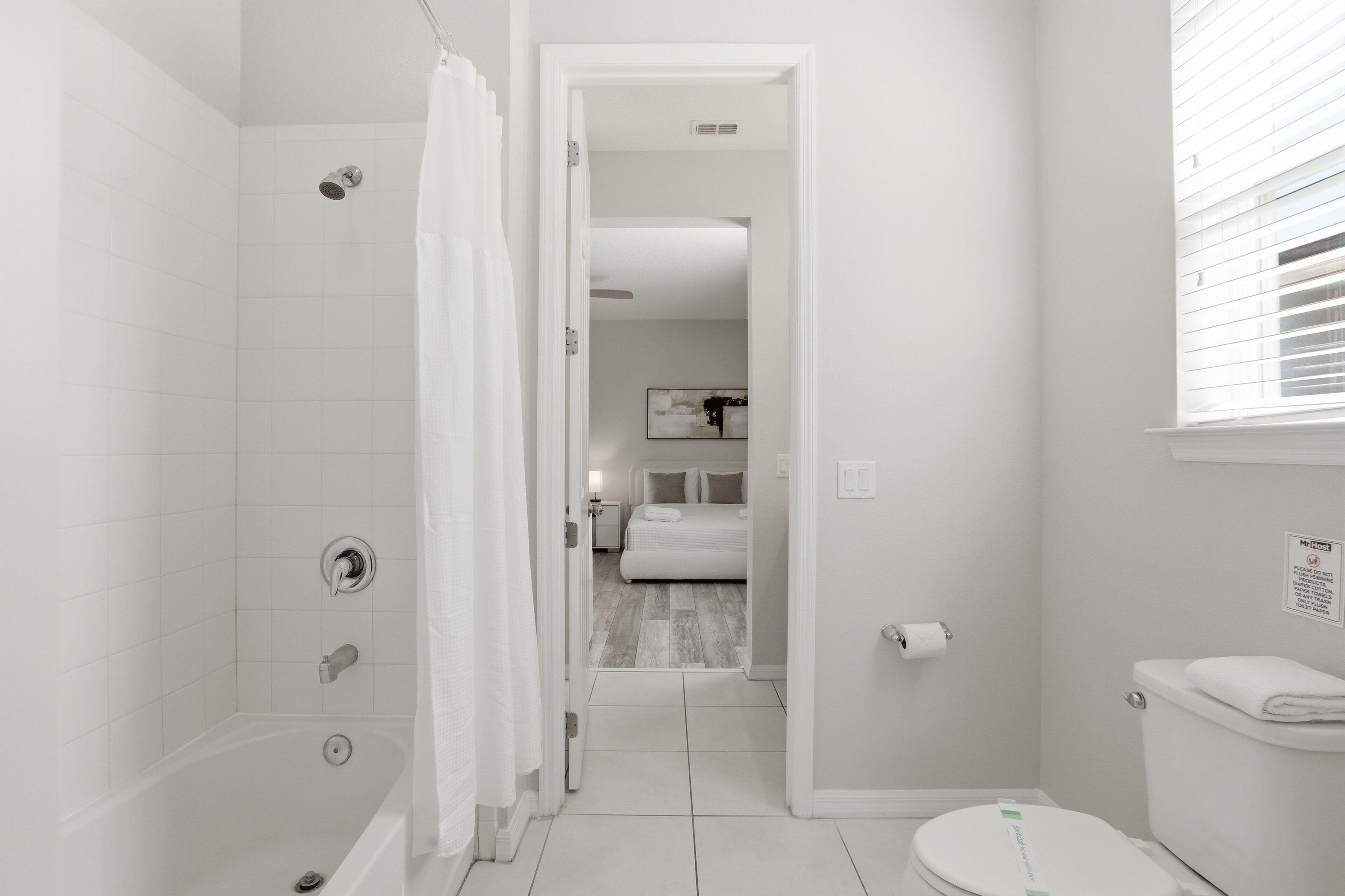 Un baño con ducha, inodoro y una cama visible en la habitación contigua.