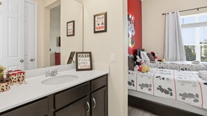 A bathroom with a white sink, dark cabinets, and a Mickey Mouse themed mirror. There are framed signs on the wall and a Mickey Mouse mural on the adjacent wall. - 7BR / 6BA w/ Private Pool / Solara Resort SO9051 (Kissimmee)