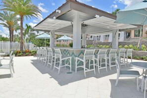 An outdoor patio area with white chairs and tables, a covered seating area, and a view of a building in the background. - 7BR / 6BA w/ Private Pool / Solara Resort SO9051 (Kissimmee)