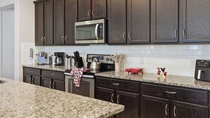A kitchen with dark wood cabinets, a stainless steel microwave, a coffee maker, and a kettle on the countertop. - 7BR / 6BA w/ Private Pool / Solara Resort SO9051 (Kissimmee)