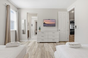 Une chambre d’hôtel avec un lit, une table de chevet, une commode, un téléviseur fixé au mur et une vue sur la plage par la fenêtre.