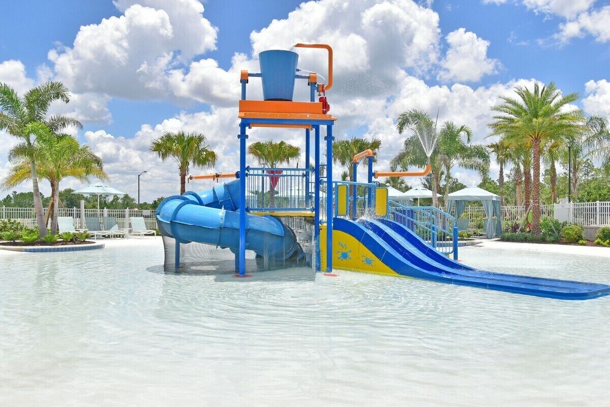 Un parc aquatique avec un toboggan bleu et jaune, des palmiers et un ciel dégagé.