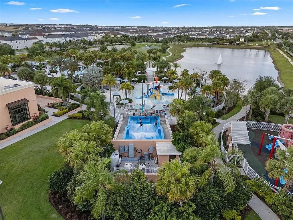 A resort with a central pool, palm trees, and a lake.