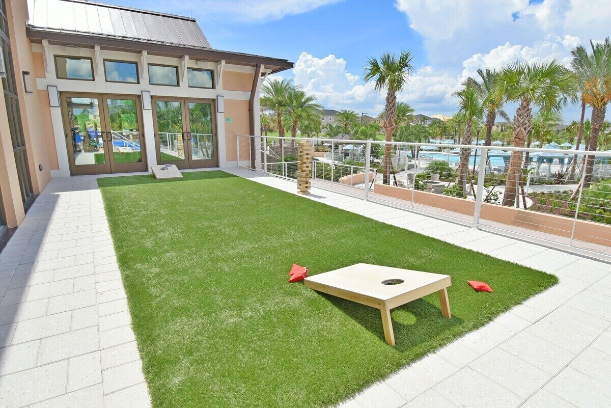 A rooftop patio with artificial grass, a wooden table, and a pool in the background.