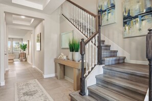 Un interior moderno con una escalera de madera, un pasillo que conduce a una sala de estar y obras de arte en las paredes.